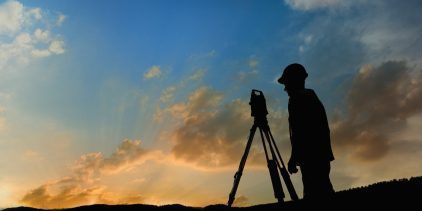 A surveyor using a total station with the sunset in the background