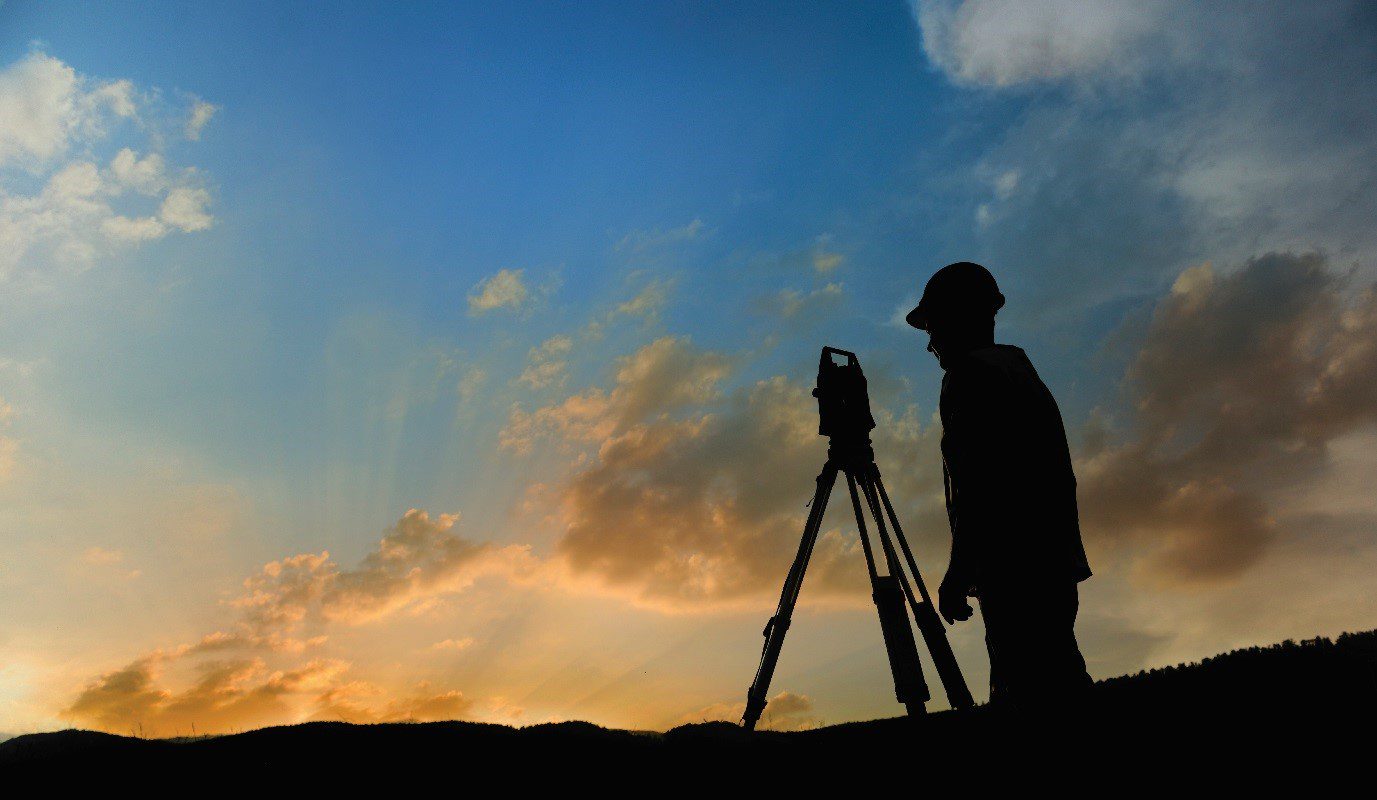 A surveyor using a total station with the sunset in the background