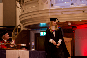 A graduate beaming on stage as she goes to collect her certificate at the December 2019 UCEM Graduation