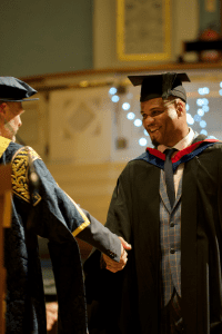 A graduate shaking hands with UCEM Principal, Ashley Wheaton, on stage at the December 2019 UCEM Graduation