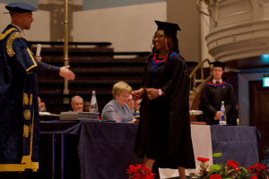 A graduate receiving her certificate on stage at the December 2019 UCEM Graduation