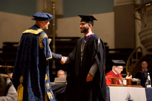 A graduate receiving his certificate on stage at the December 2019 UCEM Graduation