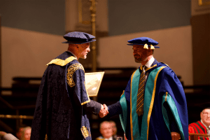 Mark Farmer receiving his Honorary Doctorate from UCEM Principal, Ashley Wheaton, on stage at the December 2019 UCEM Graduation