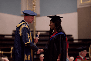 A graduate receiving her certificate on stage at the December 2019 UCEM Graduation