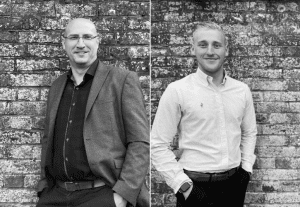 Two men stood side by side against brick wall